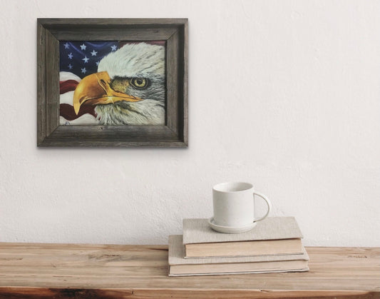 Framed print of bald eagle against a waving American flag backdrop hanging on a wall above a rustic shelf